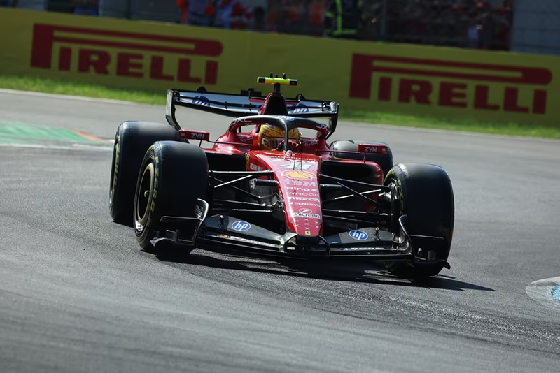 Une monoplace Ferrari de Formule 1 rouge en action sur le circuit de Monza, avec un panneau publicitaire Pirelli jaune vif en arrière-plan. La voiture, Lewis Hamilton en piste